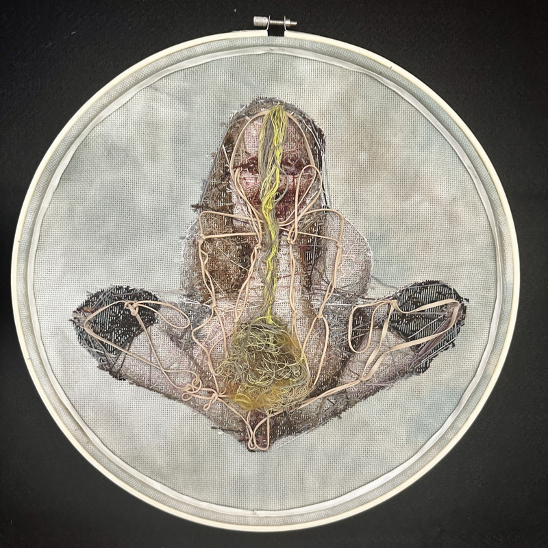 The reverse side of the piece shows the figure with a stream of yellow-green and brown thread leading from the center of their head to their abdomen in a large knotted tangle. Throughout the body of the figure, beige elastic bands have been tied together in knots and stitched to their limbs and joints. The elastic bands will dry out and crumble over time. 
